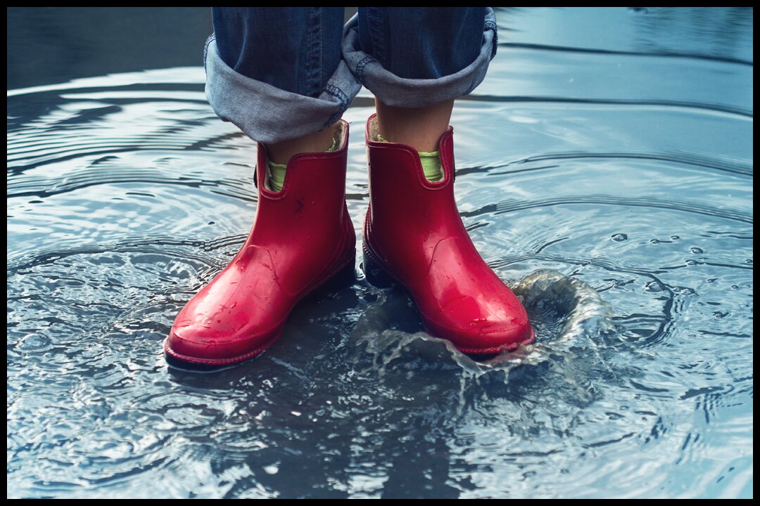 woman with red boots standing in a big puddle of water learning how heavy rain damages your roof