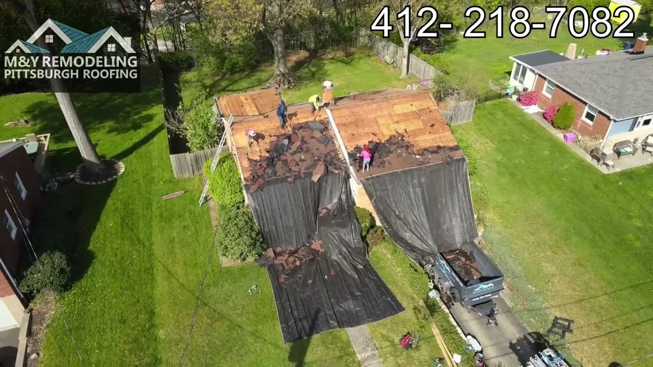 Roofing professionals tearing off shingles from a roof so it can be replaced.